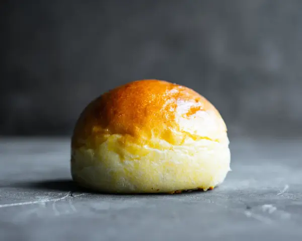 Ein goldbraunes Brioche-Brötchen liegt auf einer dunklen Oberfläche.