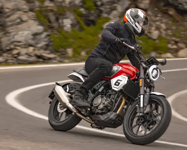 Motocyklista w kasku jedzie czerwonym motocyklem po krętej drodze. Idealny motocykl na początek przygody z jazdą.