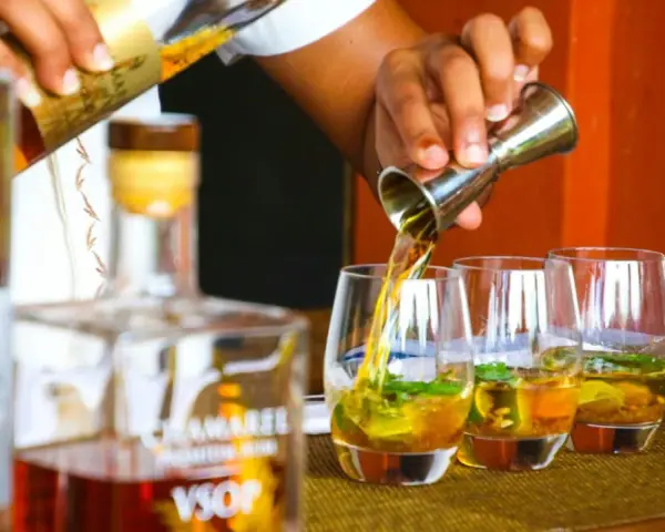 Ein Barkeeper gießt bernsteinfarbenen Rum in Gläser mit Eis und Minze. Die Frage "ab wann brennt Schnaps" wird hier durch das Servieren von edlem Rum beantwortet.