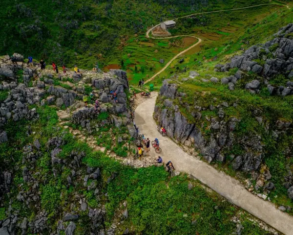Grupa rowerzystów na malowniczej trasie Ha Giang Loop, wśród skalistych zboczy i zielonych tarasów.