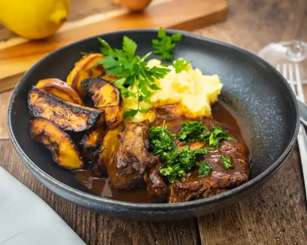 Ein Teller mit dem originalen Ossobuco-Rezept, dazu Kartoffelpüree und geröstete Kartoffelspalten.