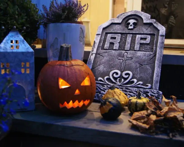 En läskig pumpa lyser upp med sitt ansikte, bredvid en gravsten och höstlöven. Perfekt för en kuslig bål halloween-kväll.
