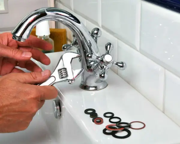 Main tenant utilise une clé pour changer un joint de robinet. Des joints sont posés sur le lavabo.