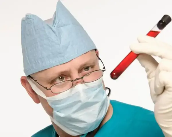 Medyk w masce i czepku ogląda probówkę z krwią. Badanie krwi to ważny element diagnostyki.