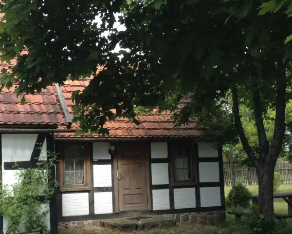 Urokliwa chata kaszubska z drewnianymi belkami i czerwoną dachówką, otoczona zielenią.