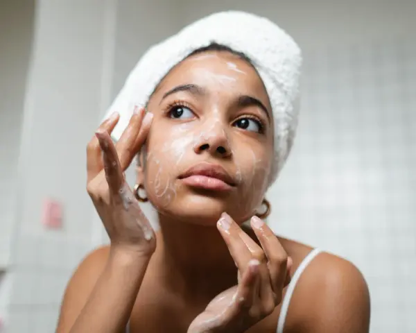 Rutina de limpieza facial: mujer con toalla en la cabeza aplica espuma en su rostro, un paso esencial para como cuidar mi piel.