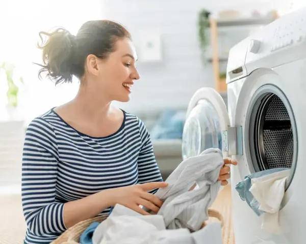 Donna sorridente carica la lavatrice, mostrando il funzionamento di un elettrodomestico moderno per il bucato.
