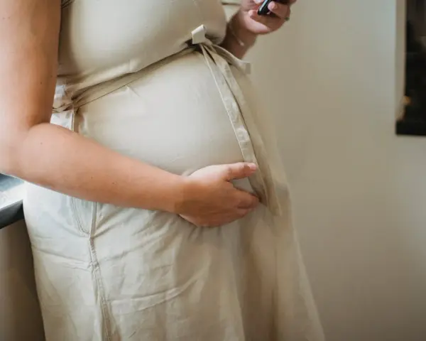 Ciężarna kobieta w beżowej sukience, która dba o zdrowie swoje i dziecka, rozważa suplementację: olej lniany w ciąży.