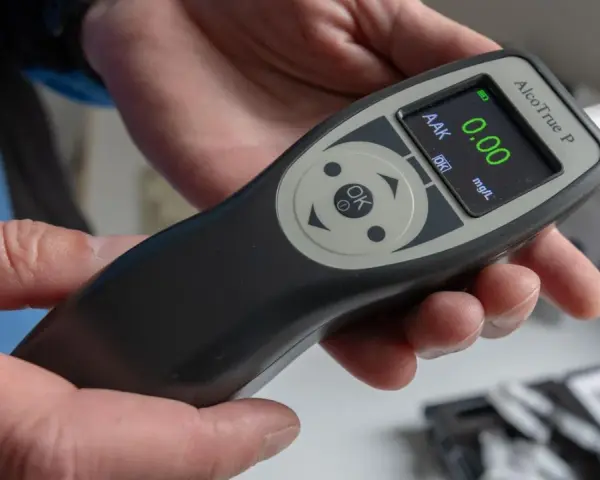 Hände halten ein Alkoholtestgerät, das 0.00 mg/L anzeigt. So vermeidet man eine Strafe wegen Alkohol am Steuer.