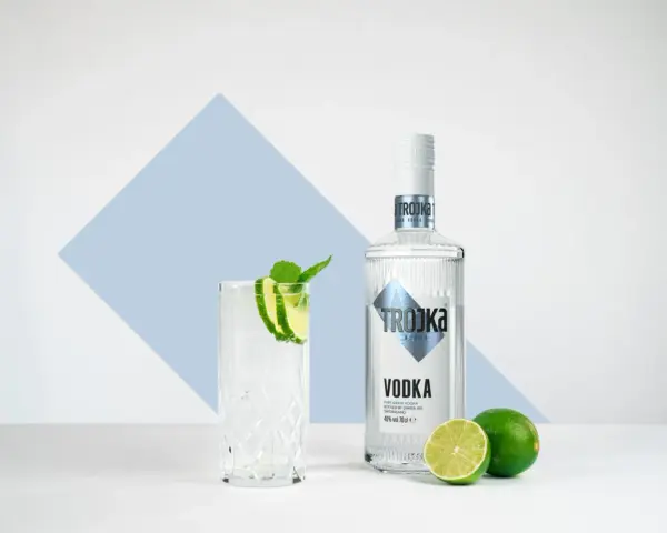 Ein Glas mit Eis, Limette und Minze steht neben einer Flasche Trojka Wodka. Perfekt für einen erfrischenden Wodka mit Wasser.