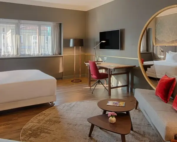 Modern hotel room with a bed, sofa, desk, and large round mirror reflecting the room.