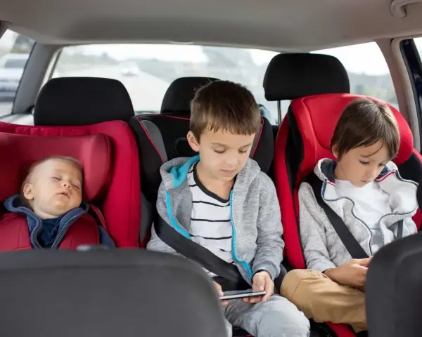 Dzieci w fotelikach samochodowych. Maluch śpi, starsi grają na telefonach. Zastanawiasz się, od jakiego wzrostu bez fotelika można podróżować?