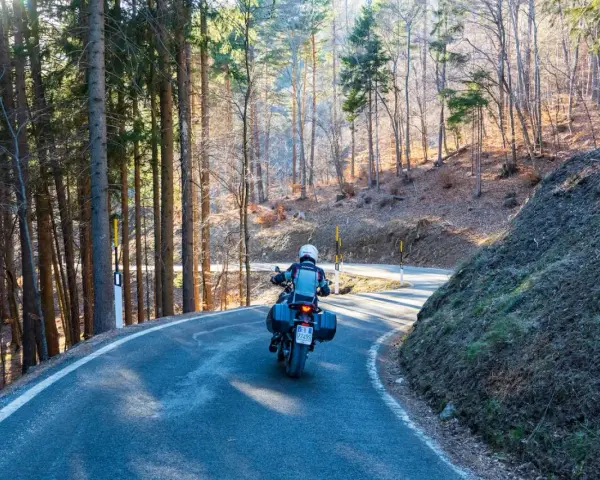 Motociclista su strada tortuosa tra i boschi, un'avventura **rund um den Gardasee**.