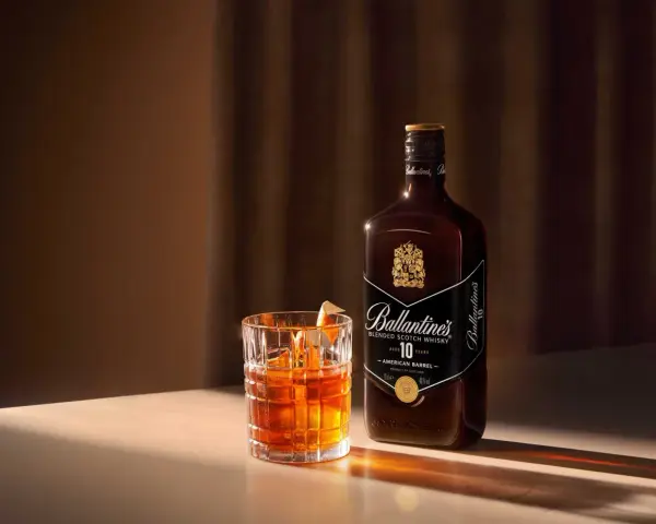 Elegancki drink Rob Roy z whisky Ballantine's 10 Year Old, podany w szkle z lodem i skórką pomarańczy.