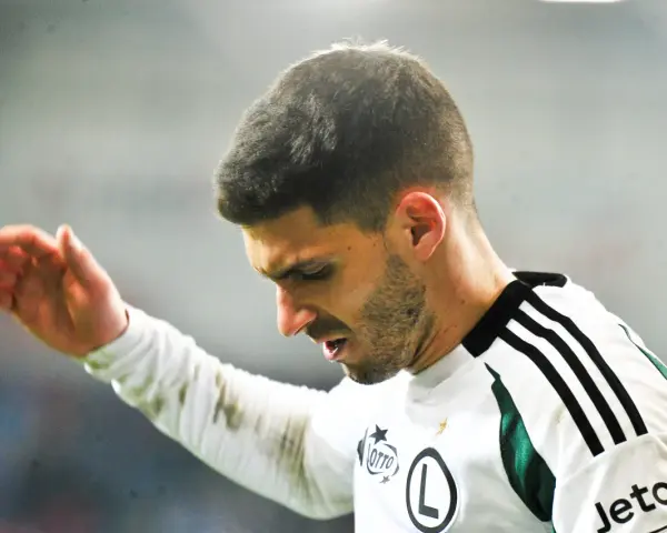 Piłkarz w białej koszulce z czarnymi pasami na ramieniu, zastanawia się, ile zarabia piłkarz ekstraklasy.