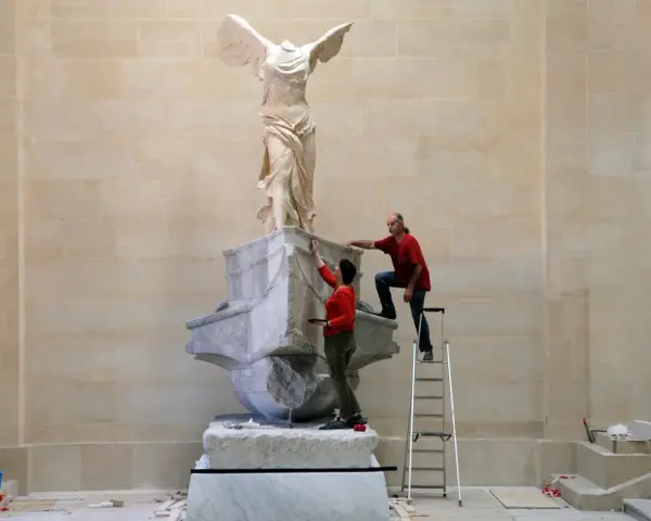 Deux personnes travaillent sur la Victoire de Samothrace, dont la signification symbolise la victoire et la liberté.