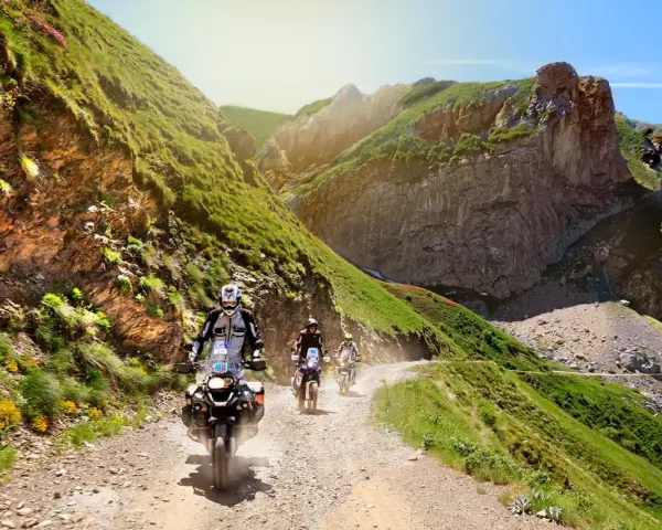 Un gruppo di motociclisti affronta un emozionante giro in moto in Liguria, su una strada sterrata tra montagne verdi e rocce imponenti.