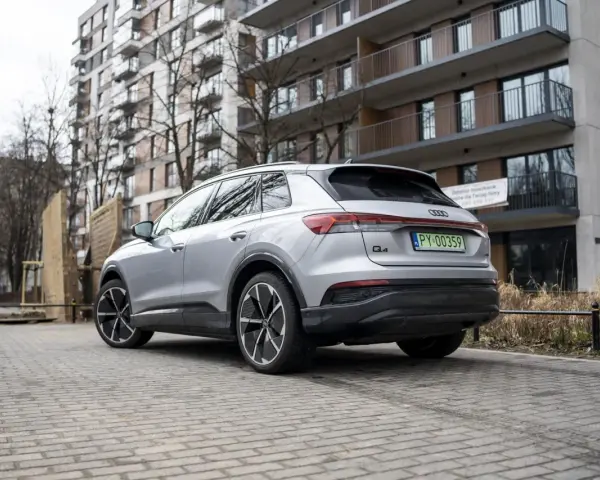 Srebrny Audi Q4 e-tron zaparkowany przed nowoczesnym budynkiem mieszkalnym.