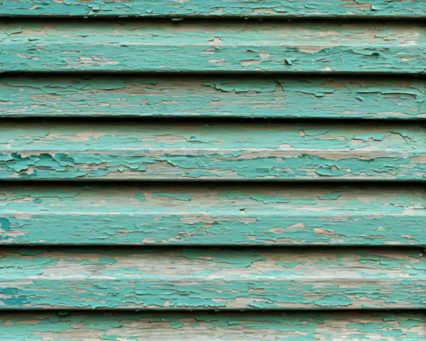 Persiane in legno fai da te con vernice verde acqua scrostata, che rivela il legno grezzo sottostante.