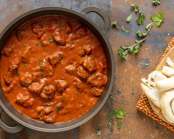 Un saporito gulash di manzo in una padella, accompagnato da pane fresco e erbe aromatiche.