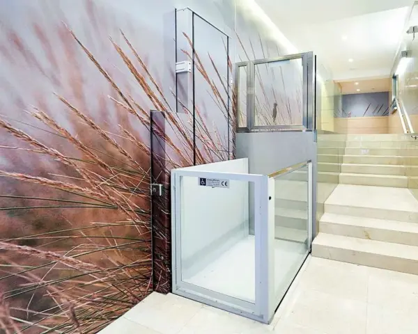 Un portal de vecinos moderno con un mural de hierbas secas y una plataforma elevadora de cristal.