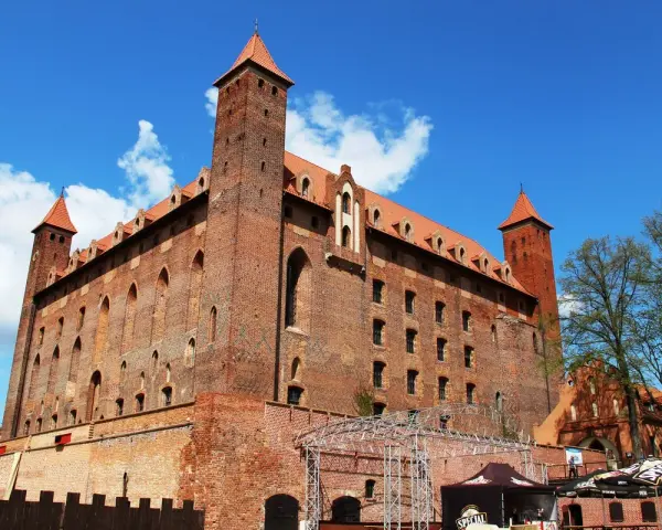Potężny zamek w Gniewie, ceglana twierdza z wieżami i czerwonymi dachami, pod błękitnym niebem. Ciekawostki o jego historii czekają na odkrycie.