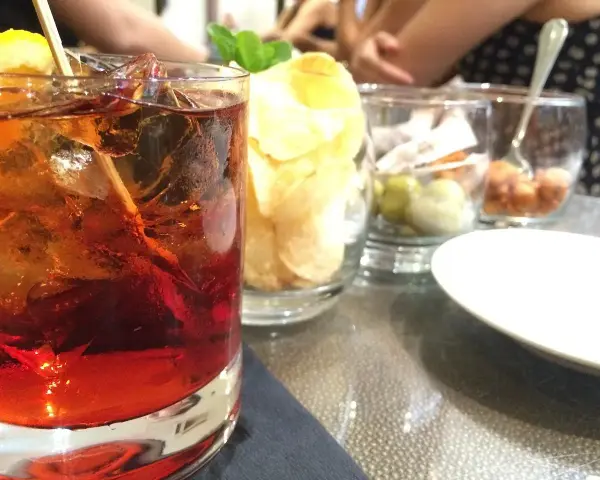 Orzeźwiający drink z lodem i cytryną, obok chipsy i oliwki. Idealne połączenie, by dowiedzieć się, **sambuca z czym pić**.