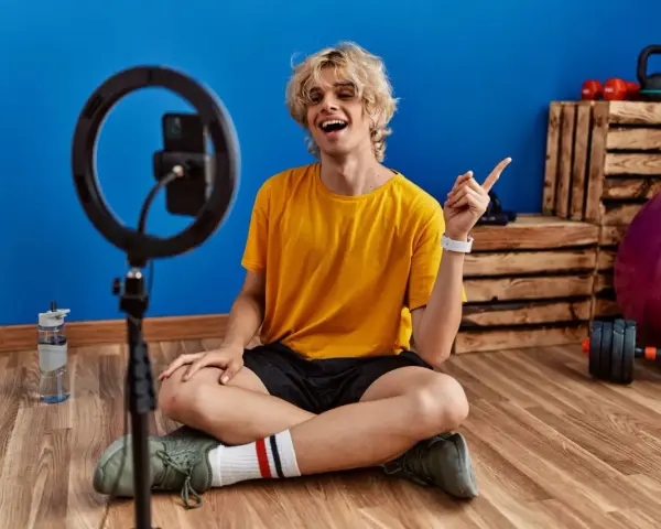 Joven influencer de fitness sonríe y señala, listo para grabar sus acciones con influencers.