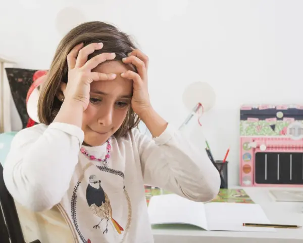 Dziewczynka z rękami na głowie, zmartwiona nauką. Jak rozładować stres u dziecka? Może zabawa?