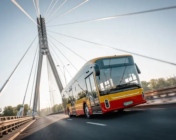 Żółto-czerwony autobus elektryczny Yutong U12 jedzie po moście nad rzeką.
