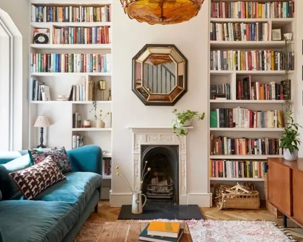 Acogedor salón estrecho y rectangular con sofá azul, chimenea y estanterías repletas de libros.