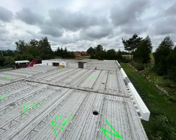 Gotowy do wylania strop, zbrojenie czeka na beton. W tle drzewa i pochmurne niebo.