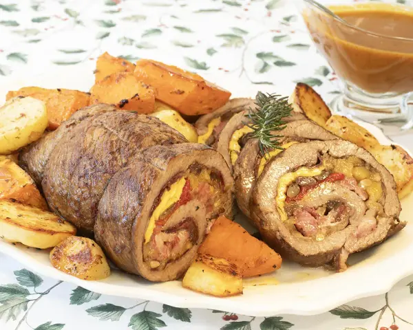 Carne asada enrollada y jugosa con papas y zanahorias asadas en un plato.
