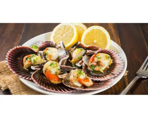 Zamburiñas a la plancha servidas en sus conchas, adornadas con perejil picado y rodajas de limón. Un plato delicioso y fresco.