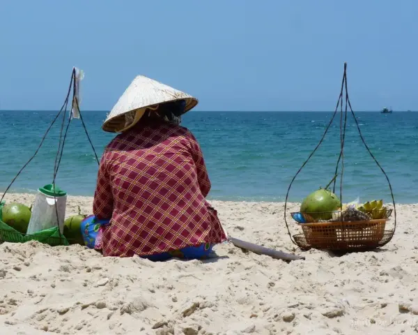 Sprzedawczyni kokosów na plaży w Mui Ne, Wietnam. W tle błękitne morze i niebo.