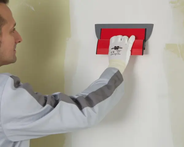 Un ouvrier utilise un outil pour appliquer une bande de placo sur un mur.