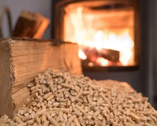 Un poêle à granulés en marche, avec des bûches et des granulés de bois à proximité. La question "peut on recharger un poêle à granulés en marche" est soulevée.