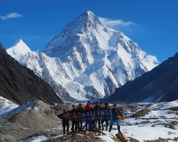 Grupa ludzi z banerem przed majestatycznym szczytem K2 w Karakorum. To wyzwanie w górach Pakistanu.