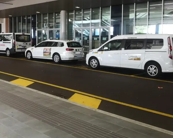 Taxi a Venezia, in attesa all'aeroporto. Diverse auto bianche, tra cui minivan e station wagon, pronte per il trasporto passeggeri.