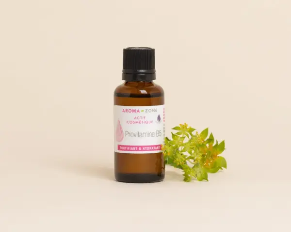 Flacone di Provitamina B5, un attivo cosmetico fortificante e idratante per la pelle, accanto a un rametto fiorito.