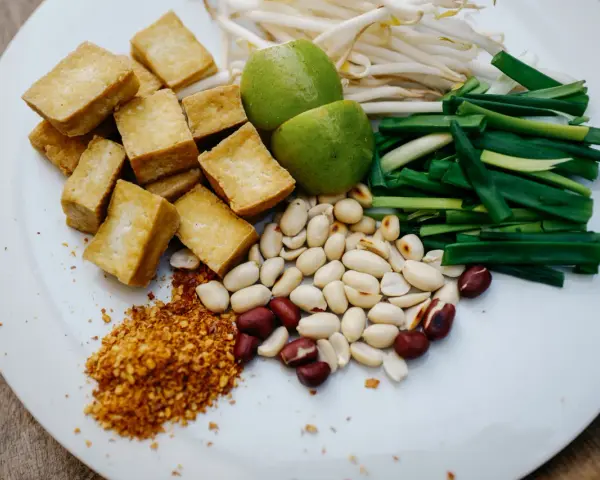 Składniki do pad ka prow: smażone kostki tofu, kiełki fasoli mung, szczypiorek, orzeszki ziemne, limonka i płatki chili.