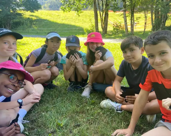 Groupe d'enfants souriants assis dans l'herbe, certains tenant des cartes.