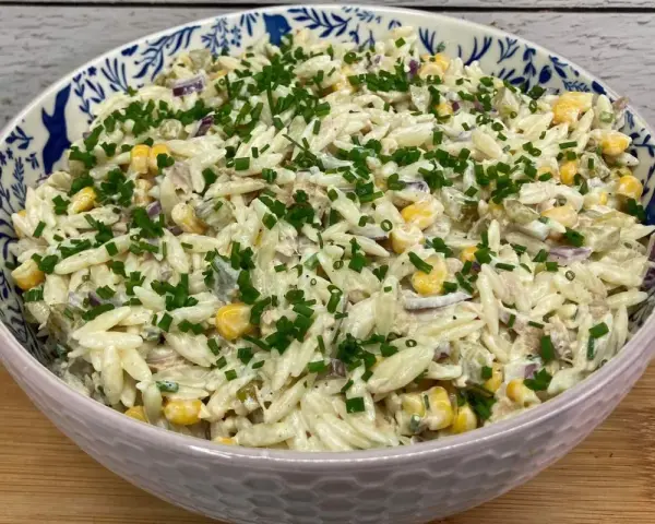 Pyszna sałatka z tuńczykiem i makaronem orzo, z kukurydzą i szczypiorkiem, w ozdobnej misce.