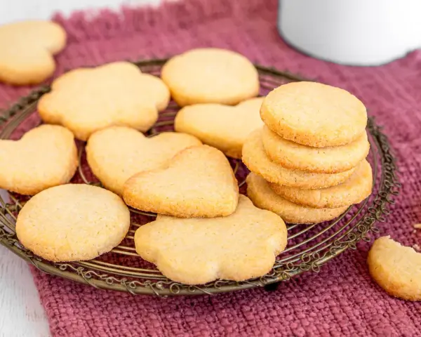 Deliziosi dolci da fare in casa, biscotti a forma di cuore e fiori su un vassoio di metallo, adagiati su un panno color prugna.