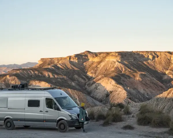 Ein Campervan steht in der Wüste Spaniens, bereit für wildcampen. Die Sonne beleuchtet die zerklüfteten Berge im Hintergrund.