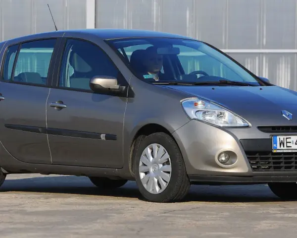 Szary Renault Clio 3 z kierowcą za kierownicą, zaparkowany na zewnątrz.