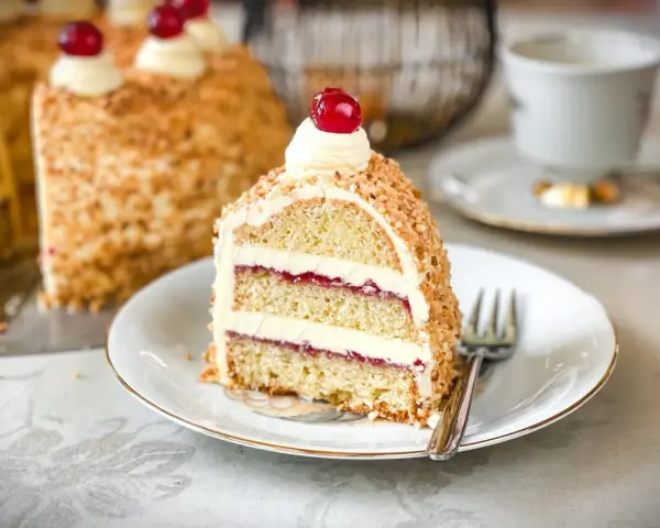 Ein Stück einer köstlichen Torte mit Buttercreme und roter Marmelade, umhüllt von gehackten Nüssen. Perfekt für die besten Torten Rezepte!