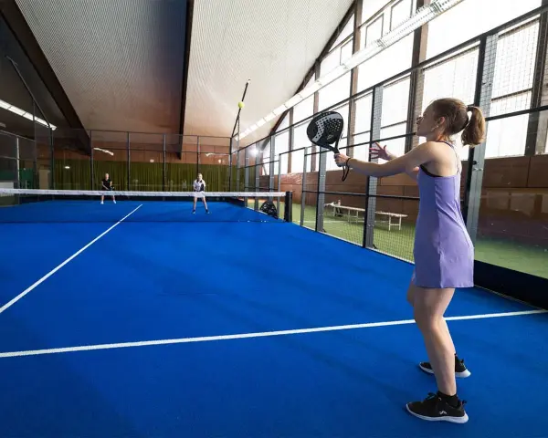 En kvinna i lila klänning spelar padel. Hon är redo att slå bollen på den blå banan.