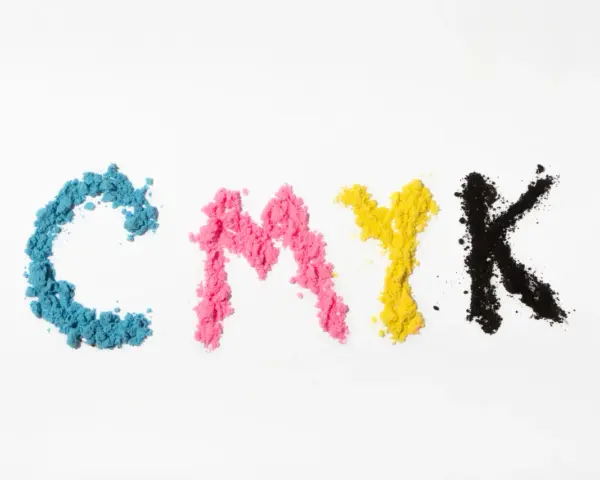 Litery CMYK ułożone z kolorowego proszku. Kolejność kolorów: cyjan, magenta, żółty, czarny.