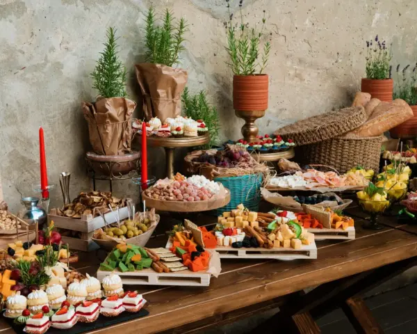 Stół z bogatym cateringiem: sery, wędliny, owoce, słodkości i pieczywo.